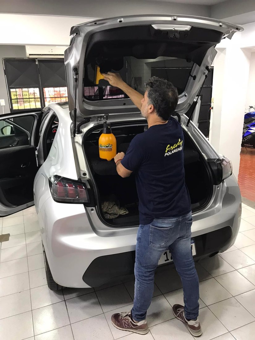 Fredy colocando la película polarizada en la luneta de un Peugeot 208 dentro del taller