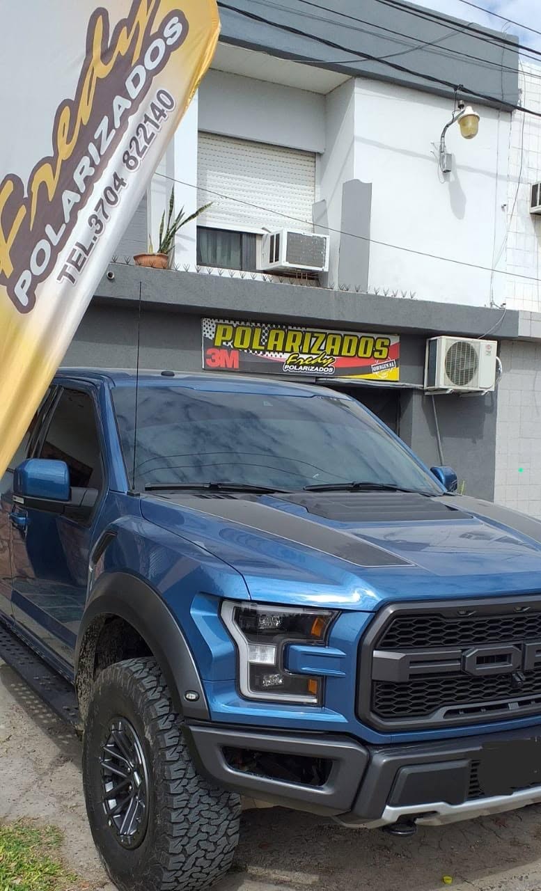 Ford F-150 Raptor azul con cristales polarizados, frente al local de Fredy Polarizados